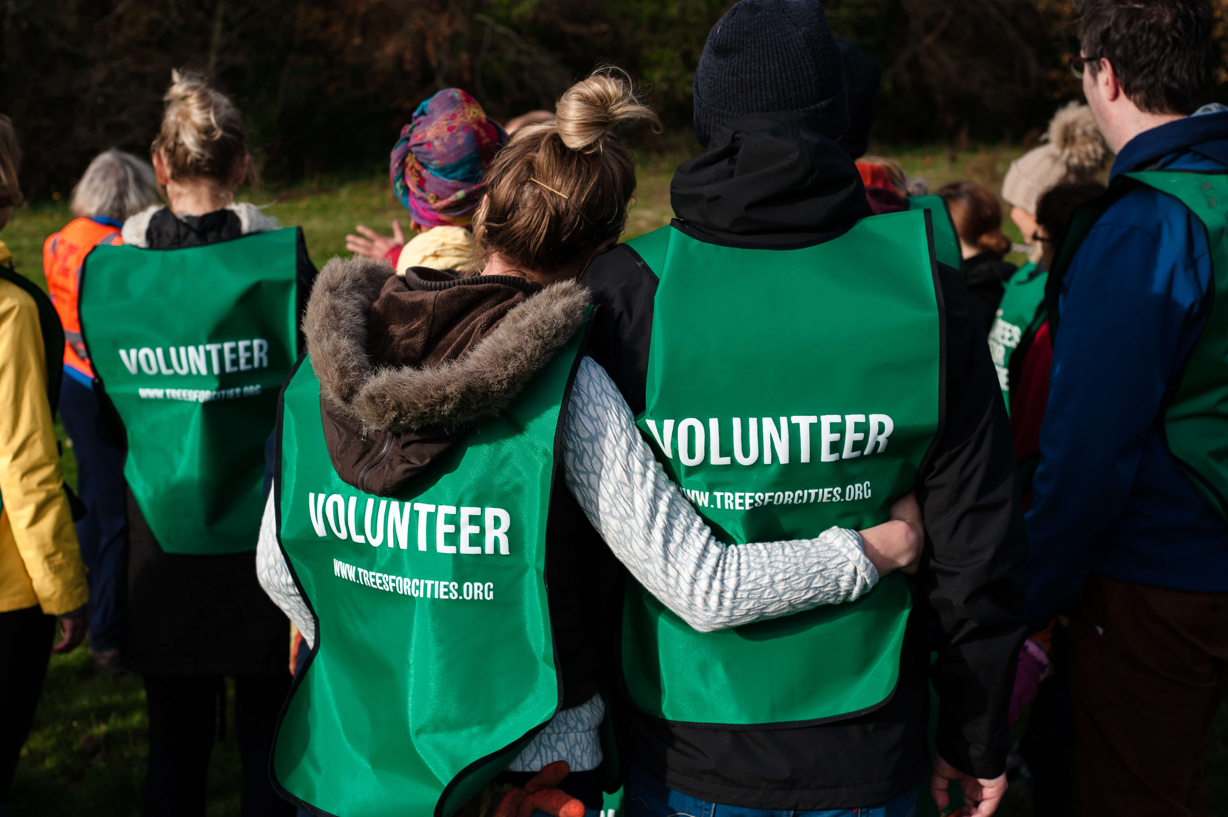 people hugging wearing trees for cities volunteer vests